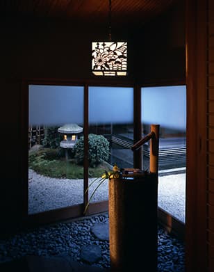 平田館の別棟にある和風の庭園を望む風景。石灯籠と庭石が配置された落ち着いた空間で、窓越しに庭が見えます。